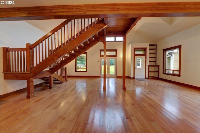 unfurnished living room with beam ceiling, light wood-type flooring, and high vaulted ceiling