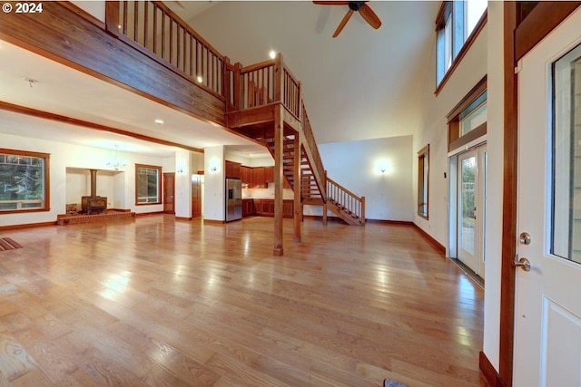 living room with a wood stove, ceiling fan, light hardwood / wood-style floors, and a high ceiling