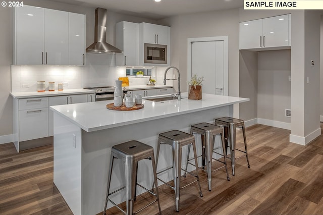 kitchen featuring appliances with stainless steel finishes, sink, an island with sink, wall chimney exhaust hood, and white cabinets