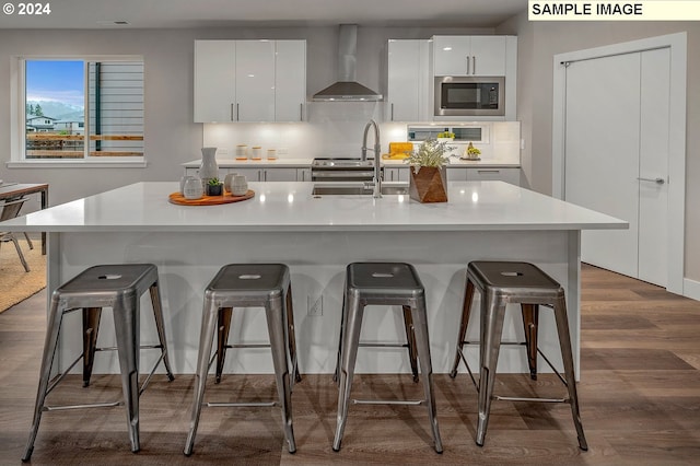 kitchen with wall chimney exhaust hood, white cabinetry, stainless steel microwave, and a breakfast bar