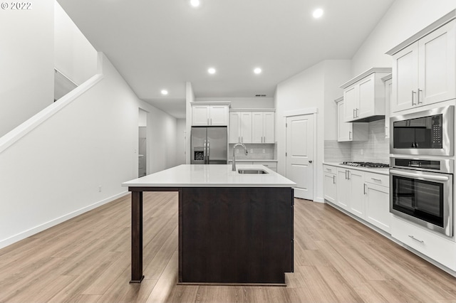 kitchen with sink, light hardwood / wood-style flooring, backsplash, a kitchen island with sink, and appliances with stainless steel finishes