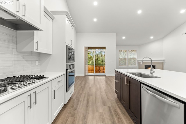 kitchen with sink, stainless steel appliances, dark brown cabinets, white cabinets, and light wood-type flooring