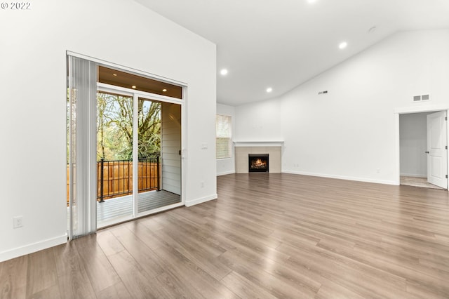 unfurnished living room featuring a tile fireplace, high vaulted ceiling, and light wood-type flooring