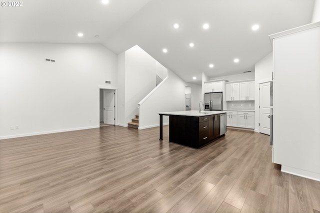 kitchen with dark brown cabinetry, stainless steel appliances, light hardwood / wood-style flooring, an island with sink, and a kitchen bar