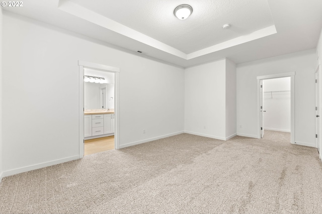 unfurnished bedroom featuring light carpet, a walk in closet, ensuite bath, a raised ceiling, and a closet