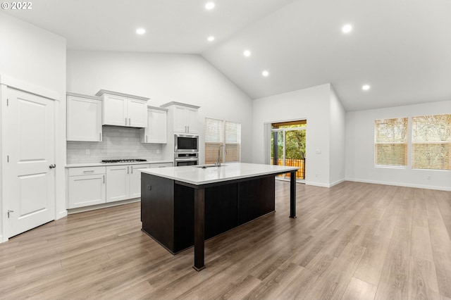 kitchen featuring stainless steel appliances, a kitchen island with sink, high vaulted ceiling, light hardwood / wood-style flooring, and white cabinets