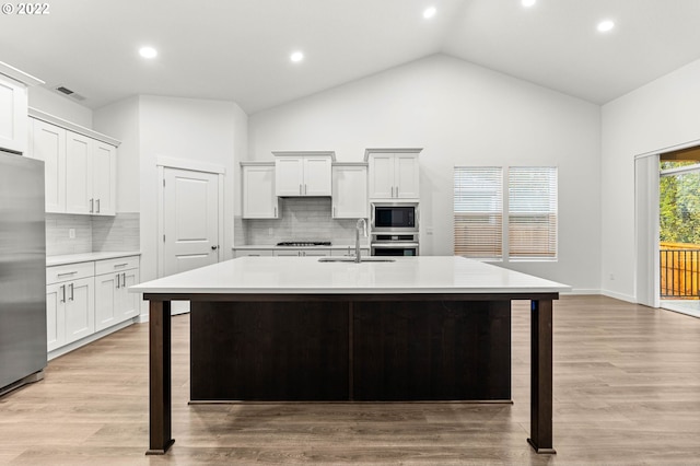 kitchen with white cabinets, light wood-type flooring, stainless steel appliances, and a kitchen island with sink