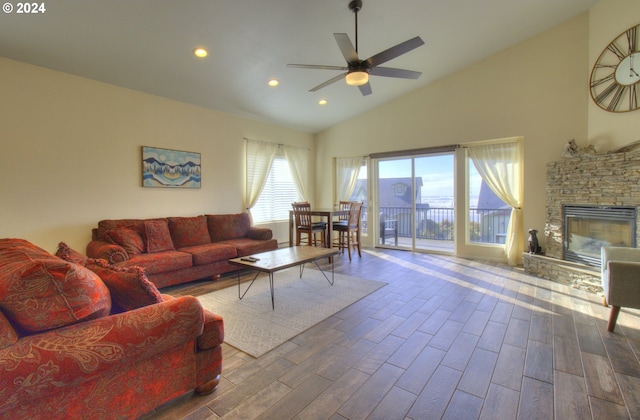 living room with hardwood / wood-style flooring, ceiling fan, a stone fireplace, and high vaulted ceiling