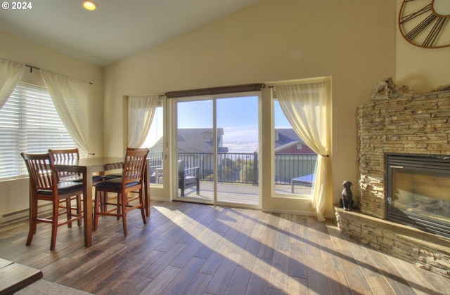 dining area featuring hardwood / wood-style flooring, a stone fireplace, and vaulted ceiling