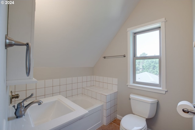 bathroom with tile patterned flooring, vaulted ceiling, a bathing tub, and toilet