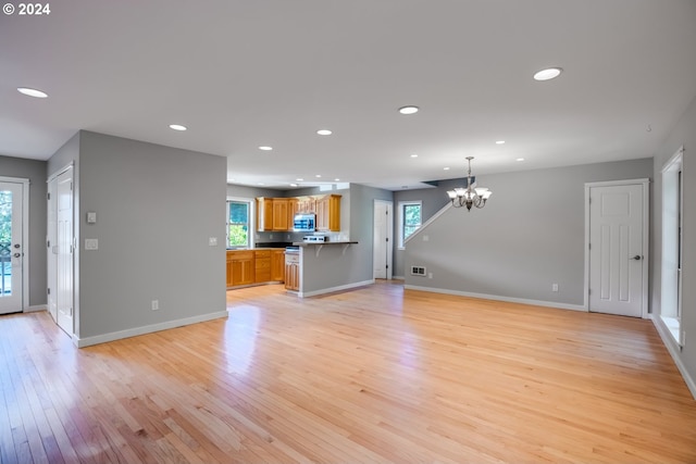 unfurnished living room featuring a wealth of natural light, a notable chandelier, and light hardwood / wood-style floors