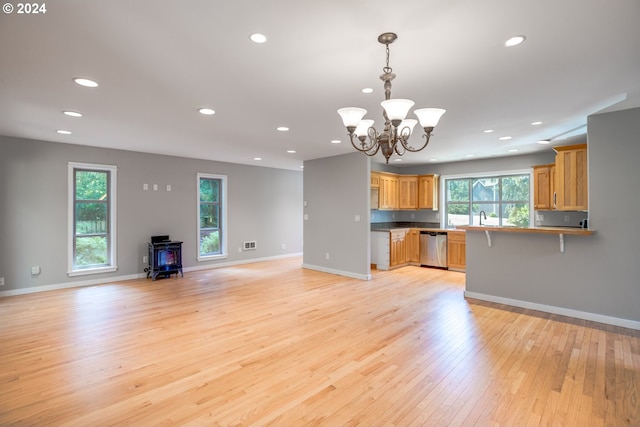 unfurnished living room with light wood-type flooring, sink, an inviting chandelier, and a wood stove