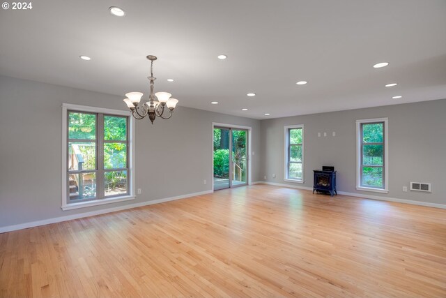 unfurnished living room featuring light wood-type flooring, an inviting chandelier, and a wood stove