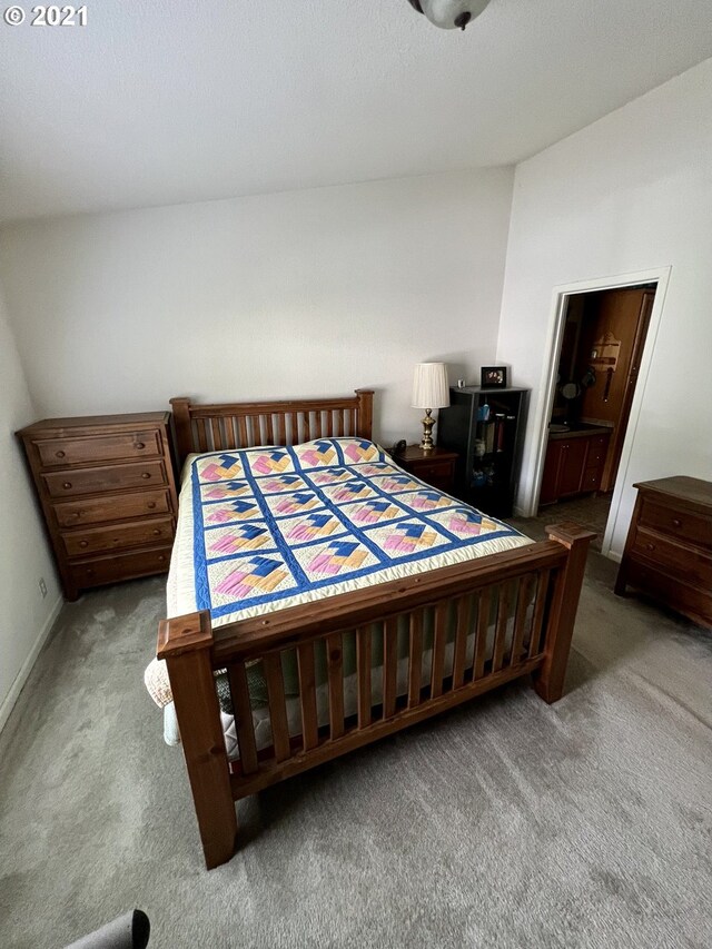 carpeted bedroom featuring lofted ceiling and ensuite bath