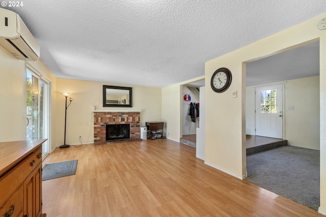 unfurnished living room with a wall mounted air conditioner, a textured ceiling, a brick fireplace, and light hardwood / wood-style flooring