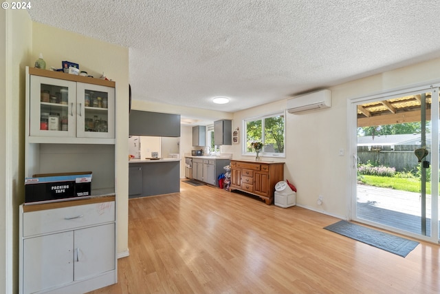 kitchen featuring gray cabinets, light hardwood / wood-style floors, an AC wall unit, and a textured ceiling