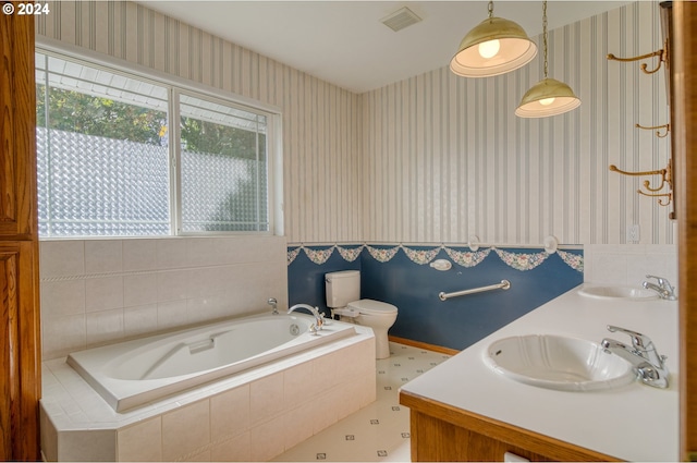 bathroom featuring tiled tub, vanity, and toilet