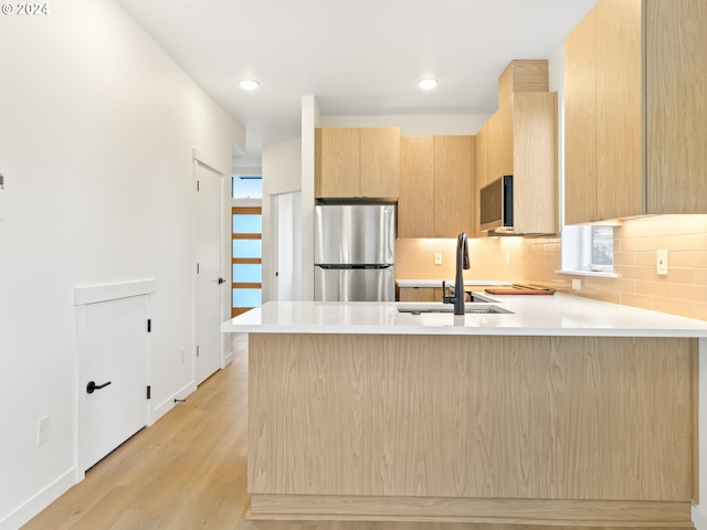 kitchen featuring sink, light brown cabinets, stainless steel appliances, light hardwood / wood-style flooring, and kitchen peninsula