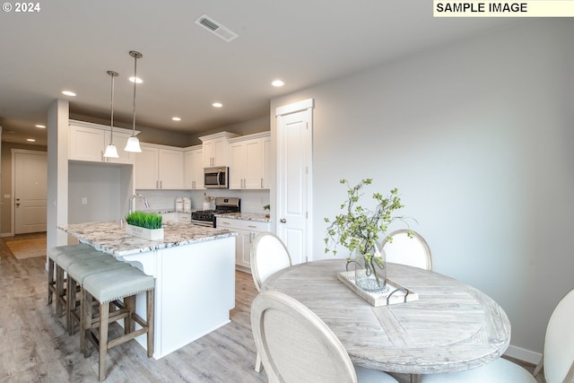 kitchen featuring decorative light fixtures, appliances with stainless steel finishes, light hardwood / wood-style flooring, white cabinetry, and a center island with sink