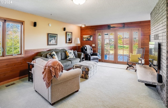 carpeted living room with wooden walls, a textured ceiling, and french doors