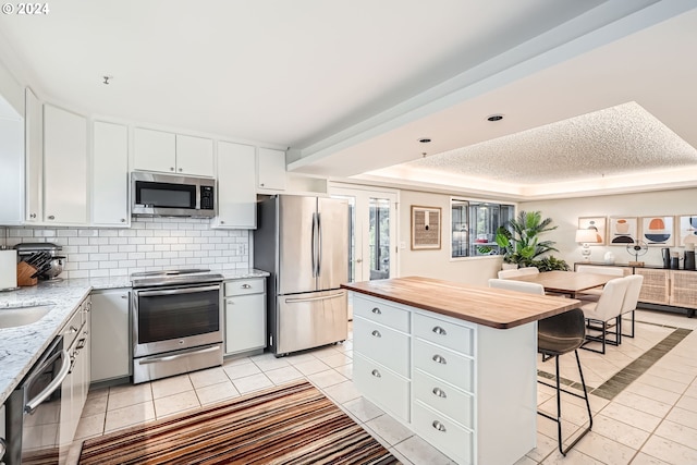 kitchen with stainless steel appliances, a kitchen breakfast bar, light tile patterned floors, a kitchen island, and white cabinets