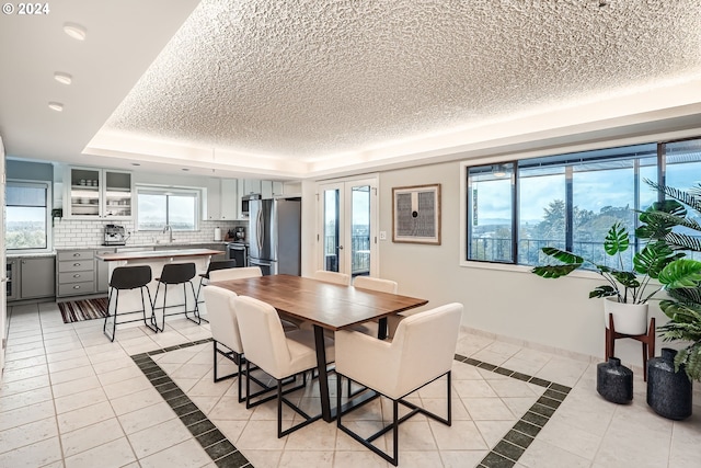 dining area featuring plenty of natural light, a textured ceiling, a tray ceiling, and light tile patterned floors