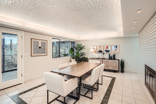 dining area with a tray ceiling, a textured ceiling, light tile patterned flooring, and a fireplace