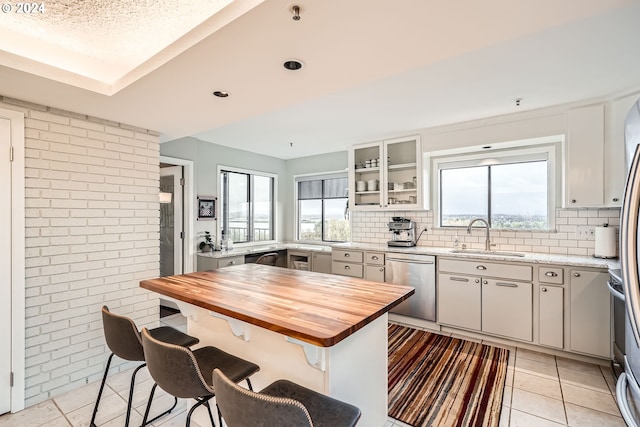 kitchen with appliances with stainless steel finishes, light tile patterned floors, sink, white cabinets, and a breakfast bar area