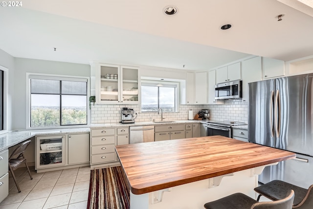 kitchen with wooden counters, tasteful backsplash, light tile patterned flooring, white cabinetry, and appliances with stainless steel finishes