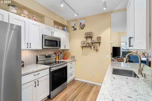 kitchen with light wood-type flooring, appliances with stainless steel finishes, light stone counters, sink, and tasteful backsplash