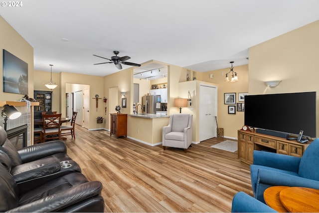 living room with sink, ceiling fan with notable chandelier, and light wood-type flooring