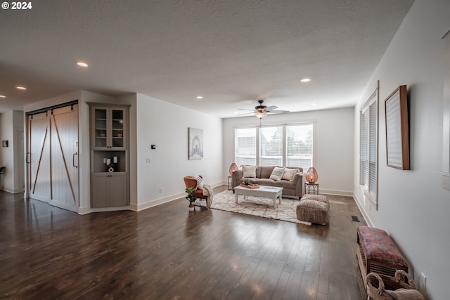 living room with a textured ceiling, ceiling fan, a barn door, and dark wood-type flooring