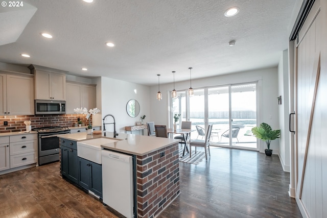 kitchen with pendant lighting, a center island with sink, sink, dark hardwood / wood-style floors, and appliances with stainless steel finishes