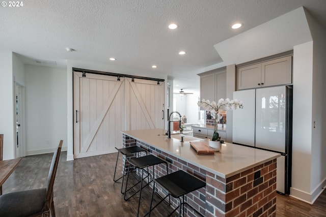 kitchen featuring dark wood-type flooring, refrigerator, gray cabinets, a barn door, and a large island