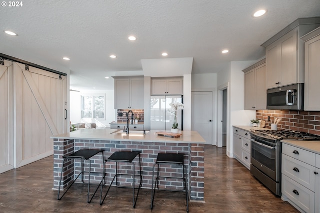 kitchen featuring a center island with sink, a barn door, stainless steel appliances, and dark wood-type flooring