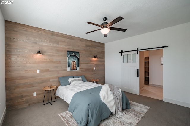 bedroom featuring carpet, ceiling fan, a barn door, and wooden walls