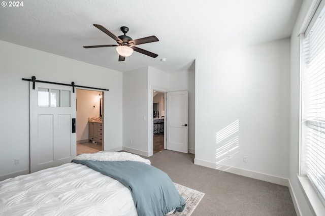 carpeted bedroom with a barn door, ensuite bathroom, and ceiling fan