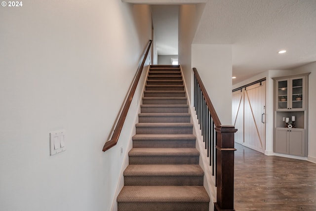 staircase with a textured ceiling, a barn door, and hardwood / wood-style flooring