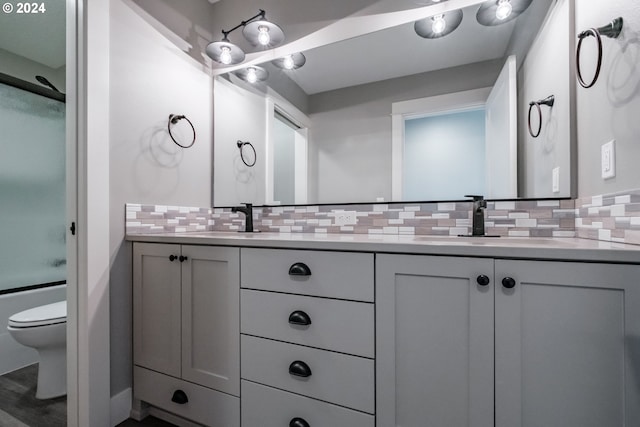 full bathroom featuring vanity, toilet, shower / bath combination with glass door, and tasteful backsplash