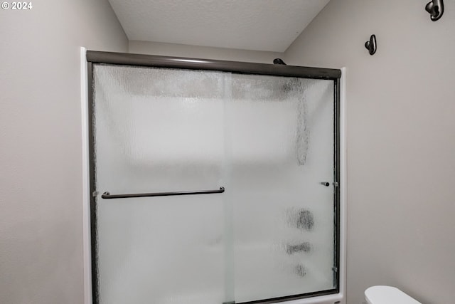 bathroom featuring toilet, a shower with shower door, and a textured ceiling