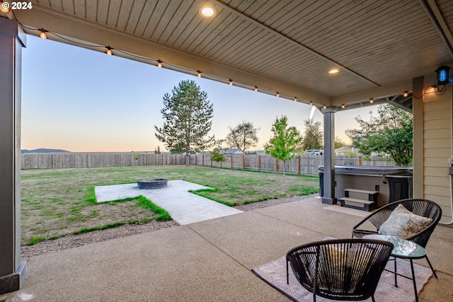 patio terrace at dusk with a hot tub, a fire pit, and a lawn