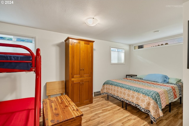 bedroom featuring a textured ceiling, light wood-type flooring, baseboard heating, and multiple windows