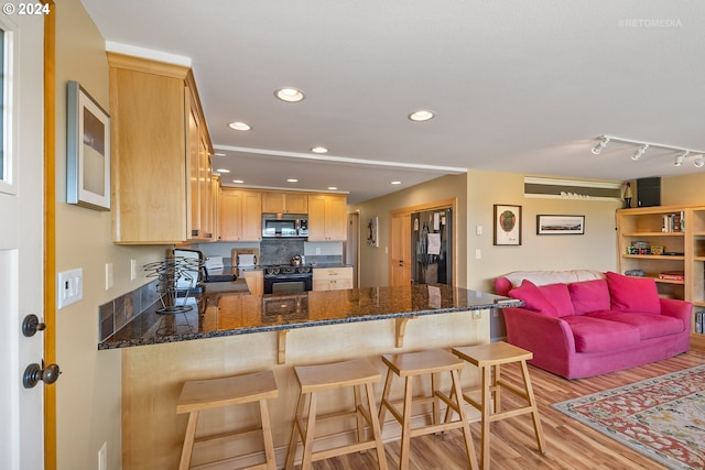 kitchen featuring light hardwood / wood-style flooring, kitchen peninsula, dark stone counters, a breakfast bar area, and black appliances