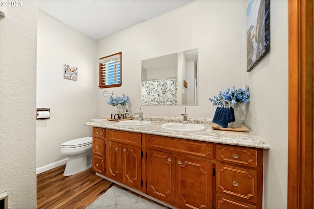 full bathroom with double vanity, a sink, toilet, and wood finished floors