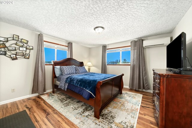 bedroom with multiple windows, baseboards, wood finished floors, and a wall mounted AC