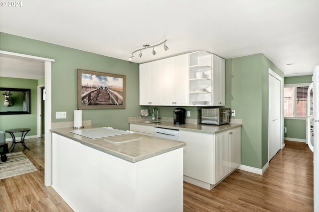 kitchen with light wood-type flooring, kitchen peninsula, sink, and white cabinets