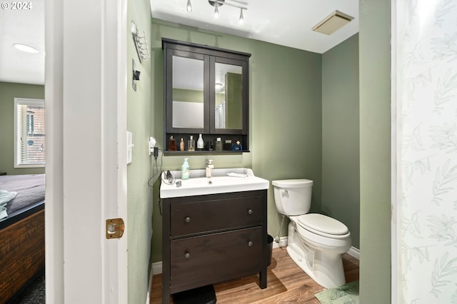 bathroom featuring visible vents, baseboards, toilet, wood finished floors, and vanity