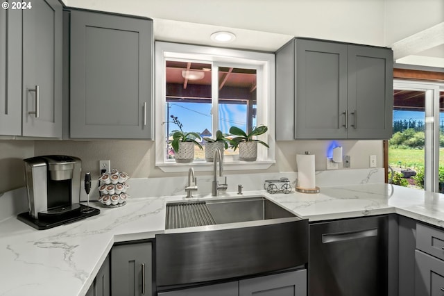 kitchen featuring light stone counters, plenty of natural light, a sink, and gray cabinetry