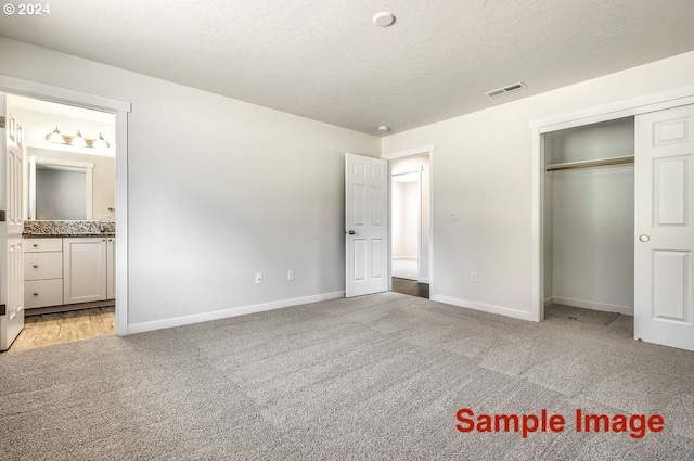 unfurnished bedroom featuring ensuite bath, light colored carpet, a textured ceiling, and a closet