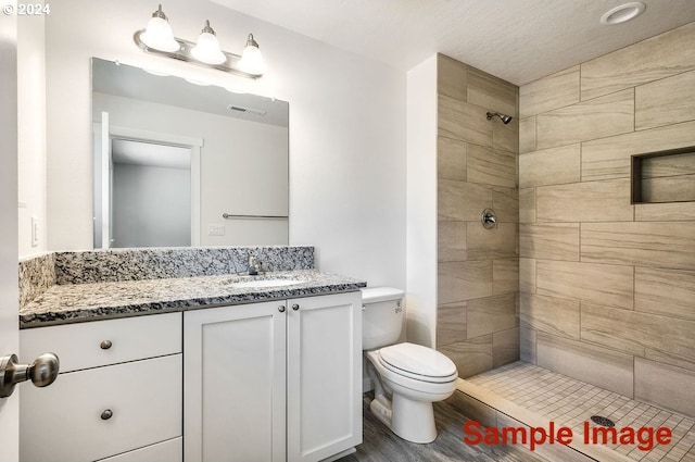 bathroom with tiled shower, hardwood / wood-style floors, vanity, and toilet